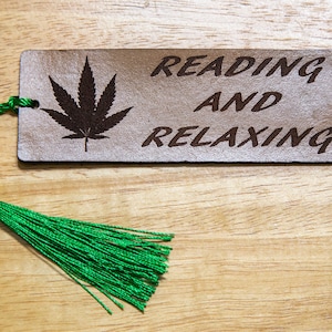 May include: A brown leather bookmark with a green marijuana leaf design and the text "Reading and Relaxing". The bookmark has a green tassel.