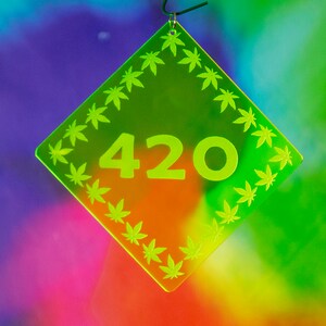 May include: A neon green, diamond-shaped decoration with the number "420" in the center. The border is lined with cannabis leaf designs. The background is a colorful blend of purple, green, and orange.