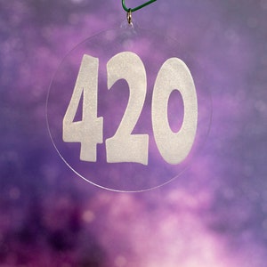 May include: A clear round ornament with the number 420 printed in white on it. The ornament is hanging from a green string.