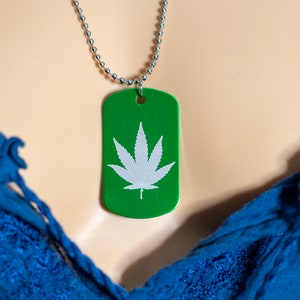 May include: A green metal dog tag necklace with a white marijuana leaf design.