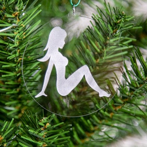 May include: A clear glass Christmas ornament with a white silhouette of a person sitting down. The ornament is hanging on a green artificial Christmas tree.