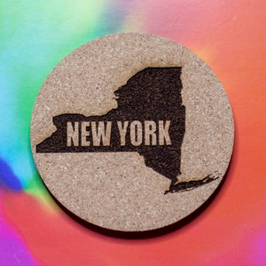Puede incluir: Un posavasos redondo de corcho con un contorno grabado con láser del estado de Nueva York y las palabras "NEW YORK" dentro del estado.
