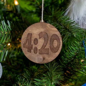 May include: A wooden Christmas ornament with the number "4:20" engraved on it. The ornament is hanging on a Christmas tree.