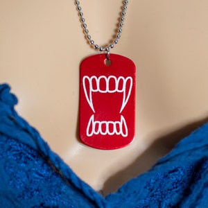 May include: A red metal dog tag necklace with a white vampire teeth design.