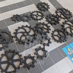 May include: A collection of black plastic gear-shaped components of varying sizes and designs, including one with a central triangle cutout. A blue product label with the text Bolt Cosplay is visible in the lower right corner of the image.