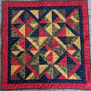 May include: A red, yellow, green, and black patchwork quilt with a geometric pattern. The quilt is framed with a red border.