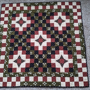 May include: A red, white, and green quilt with a checkered pattern and a star design in the center. The quilt is made of fabric squares sewn together.