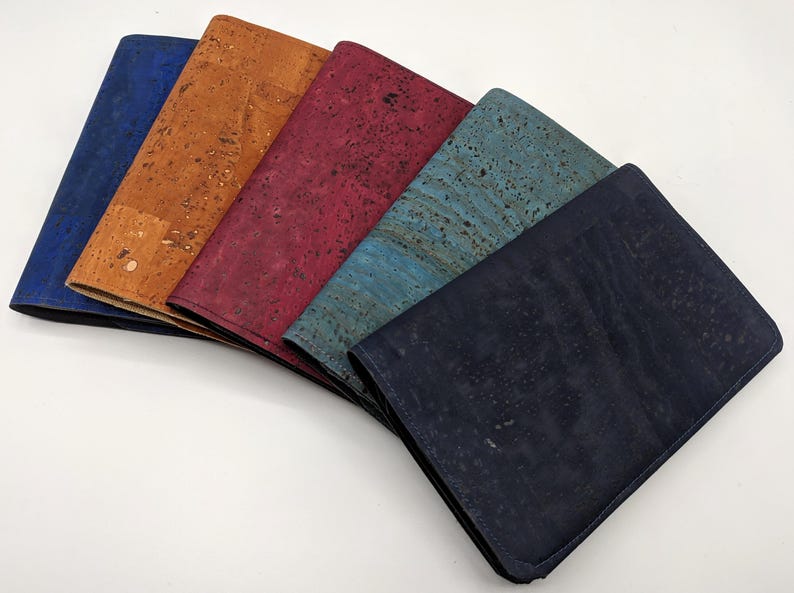 May include: Five cork wallets in different colors: blue, brown, red, teal, and black. The wallets are arranged in a fan shape, with the blue wallet on the left and the black wallet on the right.