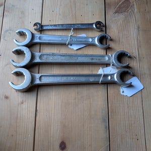 May include: A set of four silver-colored metal flare nut wrenches arranged horizontally. The top wrench is marked Snap-on 3/8 and 7/16. The three larger wrenches are marked Bonney USA with sizes 7/8, 3/4, and 1 inch visible on the metal shafts.