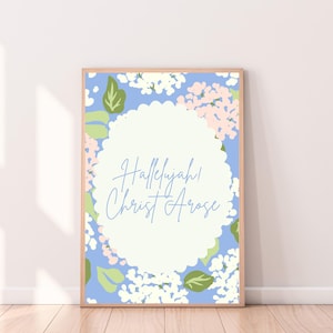 May include: A framed art print with the words "Hallelujah! Christ Arose" in a light blue script. The background features a floral pattern with white, pink, and green accents on a light blue backdrop. The frame is a light brown color.