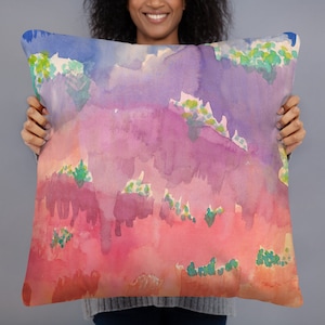 May include: A watercolor pillow cover with a pink, purple, and blue abstract design. The design features a landscape with hills and trees.