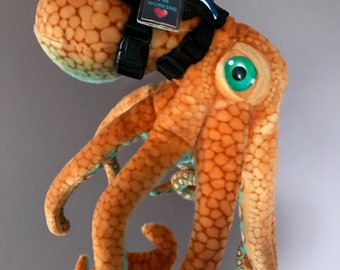May include: Orange octopus plush toy with blue accents wearing a black harness with a tag that reads "Do Not Pet I'm Working" with a red heart.