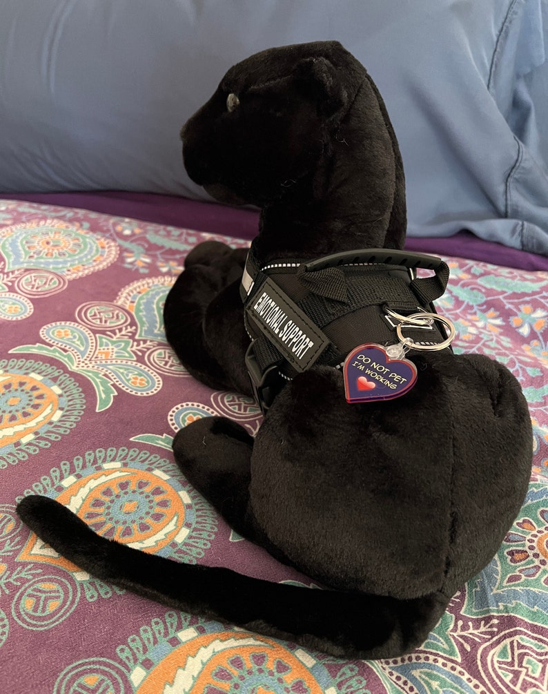 May include: Black plush toy dog wearing a black harness with the text "Emotional Support" and a red heart-shaped tag that says "Do Not Pet I'm Working".