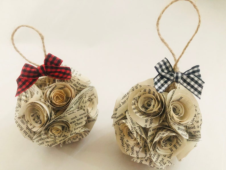 May include: Two handmade paper ornaments, each featuring a cluster of paper roses. One has a red and black plaid bow, the other a black and white plaid bow. Both have a twine loop for hanging.