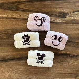 May include: Four white and purple fuzzy headbands with different Disney character designs. The designs include Mickey Mouse, Minnie Mouse, and a pirate Mickey Mouse.