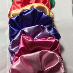 May include: Set of seven satin scrunchies in various colours, including green, red, gold, blue, purple, pink, and light pink.