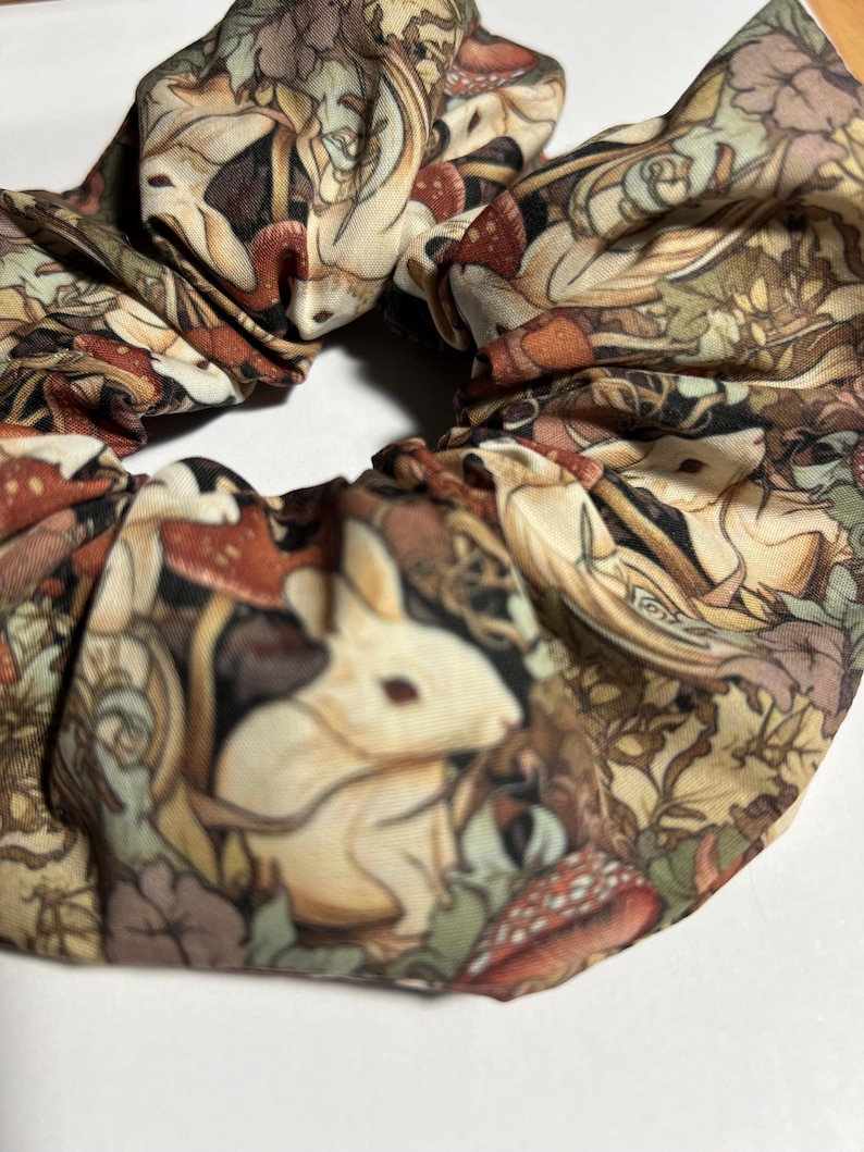 Puede incluir: Un scrunchie de tela marr&oacute;n, blanco y verde con un patr&oacute;n repetido de conejos blancos, setas y hojas.