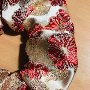 May include: A gold and red fabric hair scrunchie with a floral pattern.