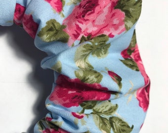 Coletero artesanal 100% algodón con estampado de rosas vintage sobre fondo azul cielo, con pompón.