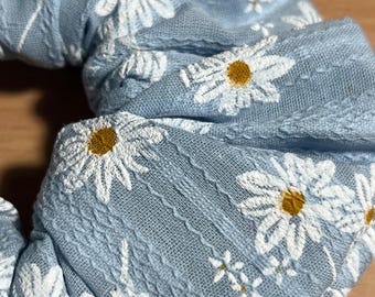 Coletero artesanal de poliéster con estampado de margaritas en azul claro y blanco, con pompón.