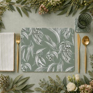 May include: A rectangular placemat featuring a sage green background with a white botanical pattern of eucalyptus leaves and gum nuts. The placemat is arranged with a gold fork, a gold knife, a matching coaster, and a striped white napkin.