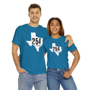 May include: Two people wearing matching teal t-shirts with a white Texas outline and the number "254" printed in black. The word "VINTAGE" is below the number. Both are wearing blue jeans.