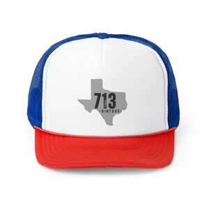 May include: A trucker hat with a white front panel, a red brim, and a blue mesh back. The front features a gray outline of Texas with the number "713" and the word "VINTAGE" printed on it.