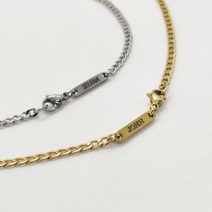 May include: Two curb chain necklaces, one silver-toned and one gold-toned, are displayed against a white background. The silver necklace has the name "SELENA" engraved on a rectangular bar. The gold necklace has the name "JOHN" engraved on a similar bar.