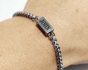 May include: A silver chain bracelet with a rectangular tag that says "JOHN" in black lettering.