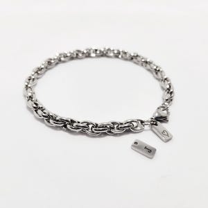 Peut inclure: Un bracelet en chaîne argent avec deux breloques argentées. Un charme a un cœur gravé dessus et l'autre charme a la lettre "J" gravée dessus.