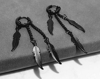 May include: A pair of black hoop earrings with dangling feather charms. Each earring features a circular hoop with a chain and three feather pendants. The earrings are displayed on a gray surface.
