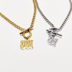 Peut inclure: Deux colliers en or et en argent avec des fermoirs à bascule et des pendentifs en forme de lettre. Le collier en or a un pendentif 'W' et le collier en argent a un pendentif 'G'.