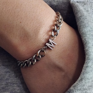 May include: A silver chain bracelet with a silver charm in the shape of the letter "M".