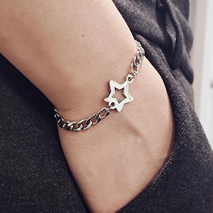 May include: A silver chain bracelet with a star-shaped charm. The chain is a curb style and the star is open in the center.