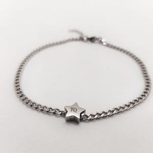 May include: A silver chain bracelet with a star charm. The star has the letters "TQ" engraved on it.