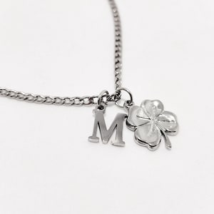 Puede incluir: Un collar de cadena de plata con un dije de letra 'M' de plata y un dije de trébol de cuatro hojas.