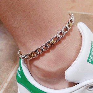 May include: A silver and gold chain anklet with a curb link design.