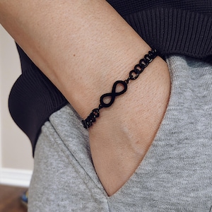 May include: A black infinity symbol charm bracelet with a chain link design.