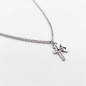 May include: A silver chain necklace with a cross pendant and a small silver tag with a cut-out design.