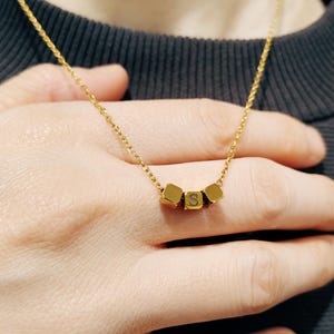 May include: A gold chain necklace with three gold cube charms, each with a letter 'S' engraved on it.