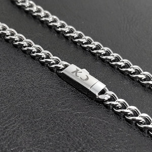 May include: A silver curb chain necklace with a clasp that has the letters "KC" engraved on it.