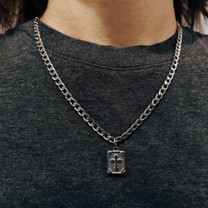 May include: A silver chain necklace with a silver pendant featuring a cross design.