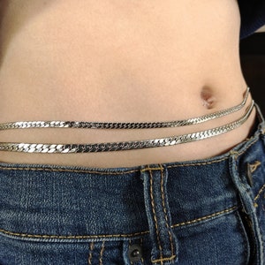 May include: A silver chain belt with two rows of links. The belt is worn around the waist and is secured with a clasp.
