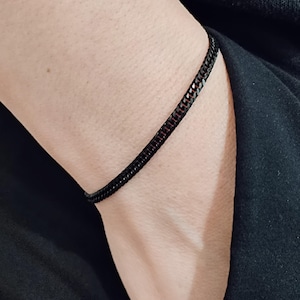May include: A black chain bracelet with a subtle red undertone. The bracelet is worn on a person's wrist.