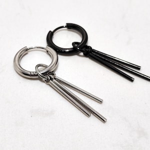 May include: Two hoop earrings, one silver-toned and one black, each with three dangling, slender bars. The earrings are displayed on a white surface, showcasing their minimalist design and contrasting colors. These earrings are suitable for everyday wear.