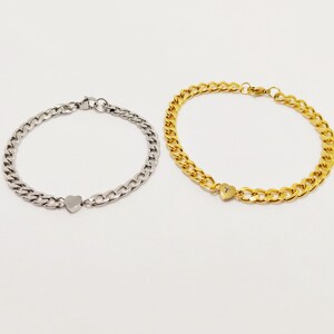 Peut inclure: Deux bracelets en chaîne avec des breloques en forme de cœur. Un bracelet est argenté et l'autre est doré.