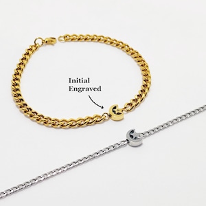 May include: Two gold and silver chain bracelets with a crescent moon charm. The gold bracelet has a curb chain design and the silver bracelet has a delicate chain design. The gold bracelet has an initial engraved on the charm.