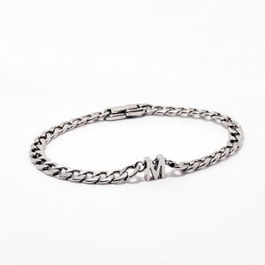 May include: A silver chain bracelet with a silver letter 'M' charm.