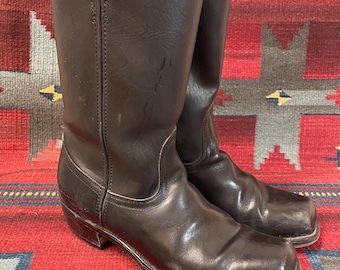 Könnte beinhalten: Ein Paar braune Cowboy-Stiefel aus Leder mit quadratischer Spitze. Die Stiefel sind hoch und haben einen leichten Absatz.
