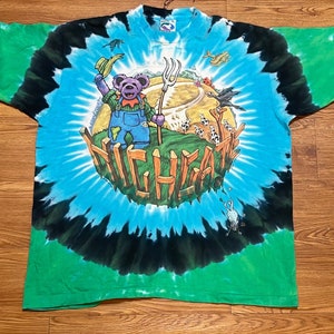 May include: A tie-dye t-shirt with a green, blue, and black swirl pattern. The shirt features a cartoon bear wearing overalls and holding a pitchfork. The text "HIGHGATE" is written in a circular pattern around the bear.